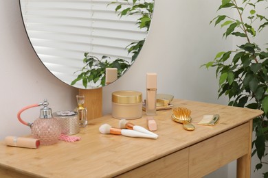 Dressing table with mirror, cosmetic products and houseplant indoors. Interior design