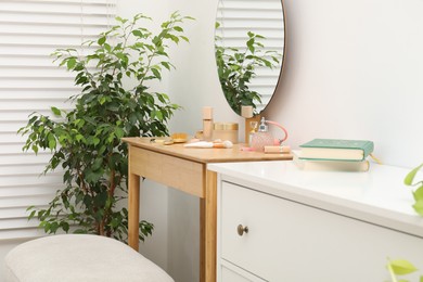 Photo of Mirror, dressing table, houseplant and chest of drawers indoors. Interior design