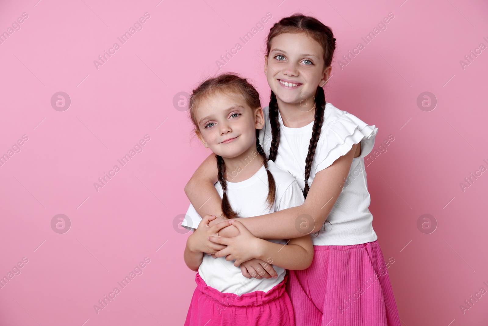 Photo of Portrait of cute little sisters on pink background, space for text