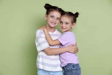 Portrait of cute little sisters on light green background