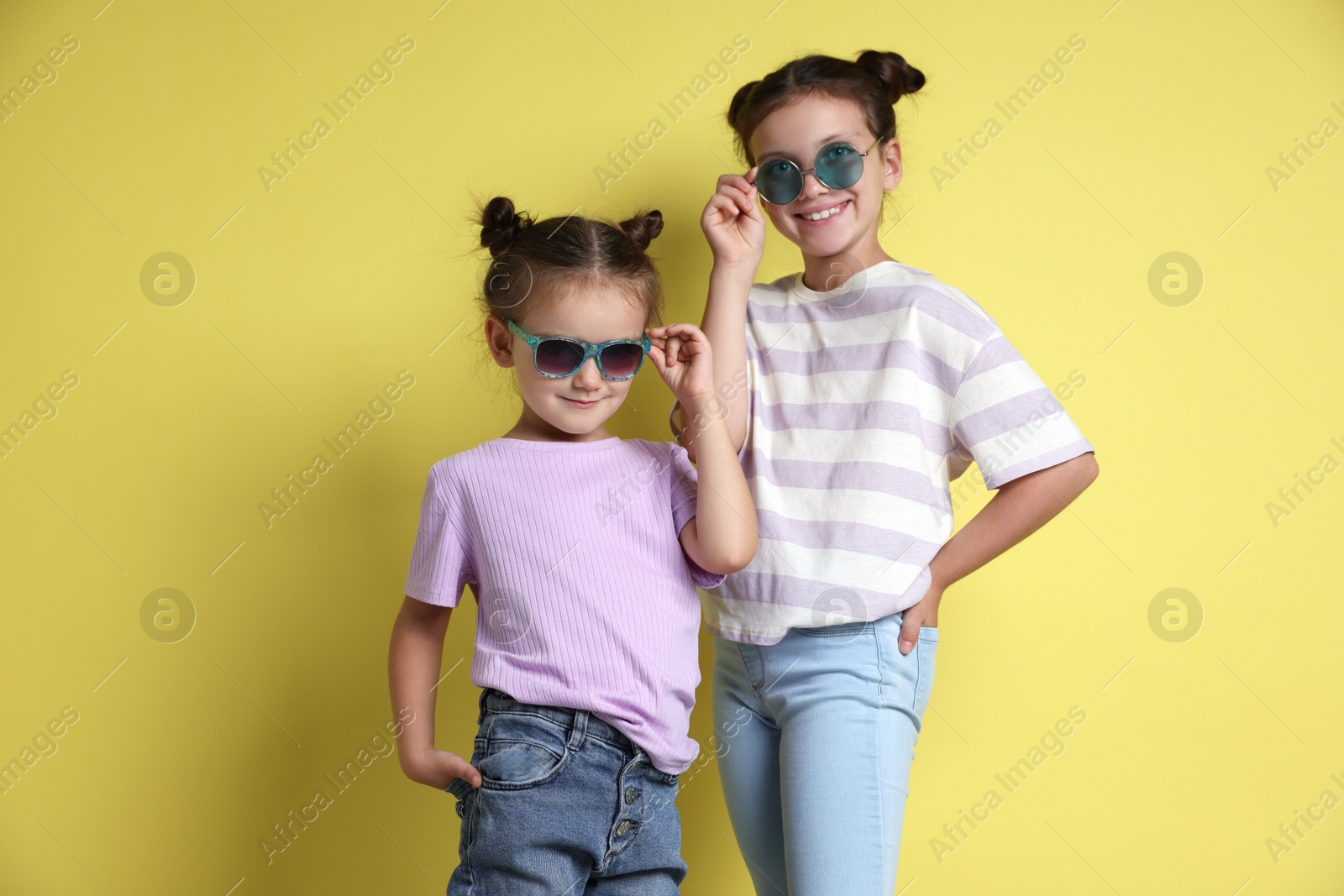 Photo of Portrait of cute little sisters on yellow background