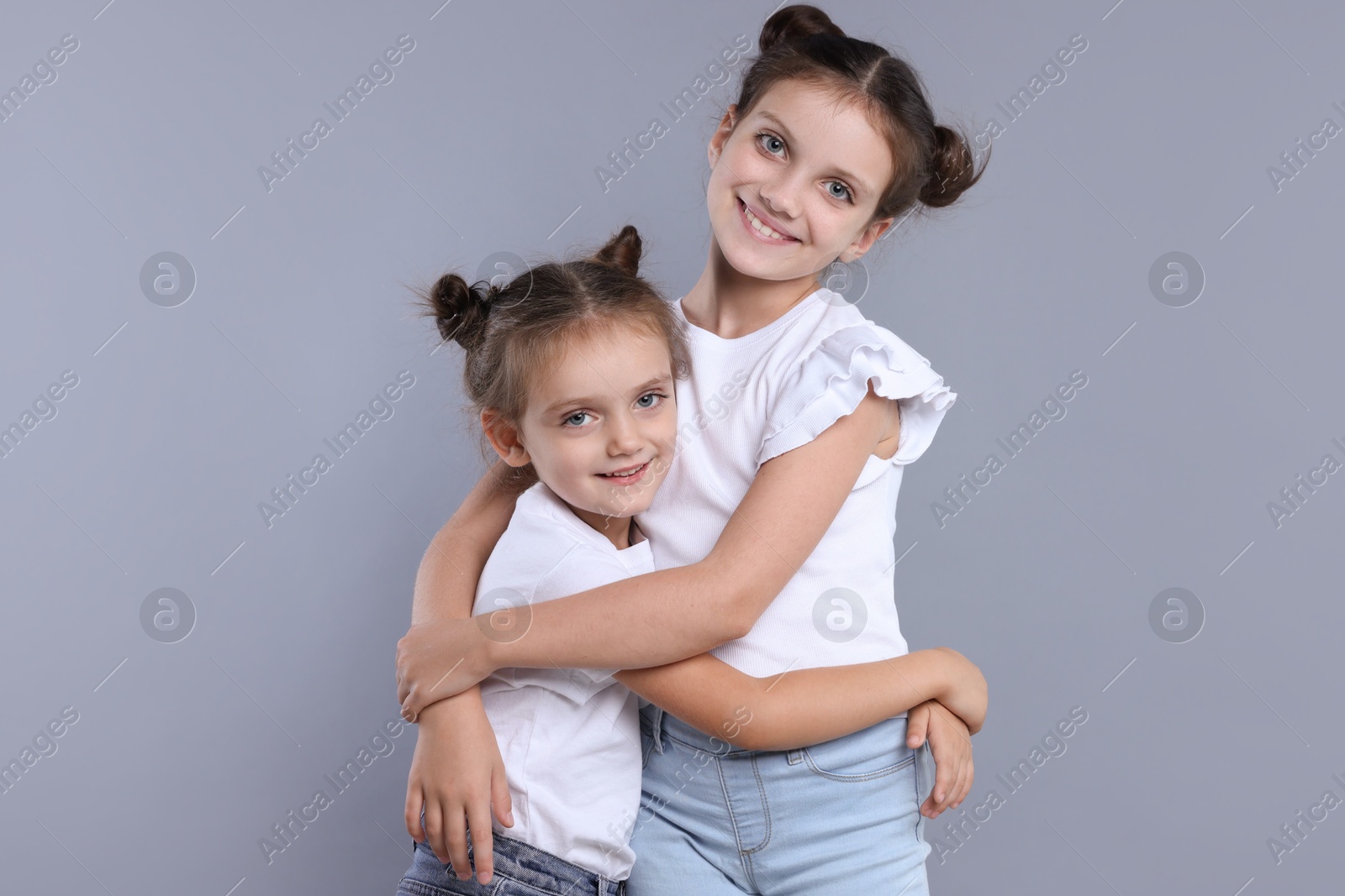 Photo of Portrait of cute little sisters on grey background