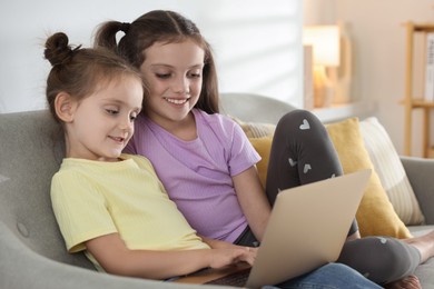 Cute little sisters with laptop spending time together at home