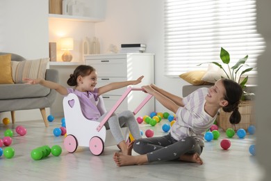 Photo of Cute little sisters playing with wooden stroller at home