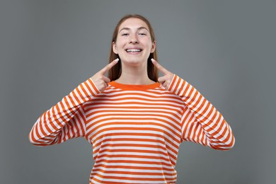 Photo of Smiling girl pointing at her braces on grey background