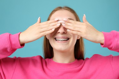 Photo of Smiling girl with braces covering eyes on light blue background