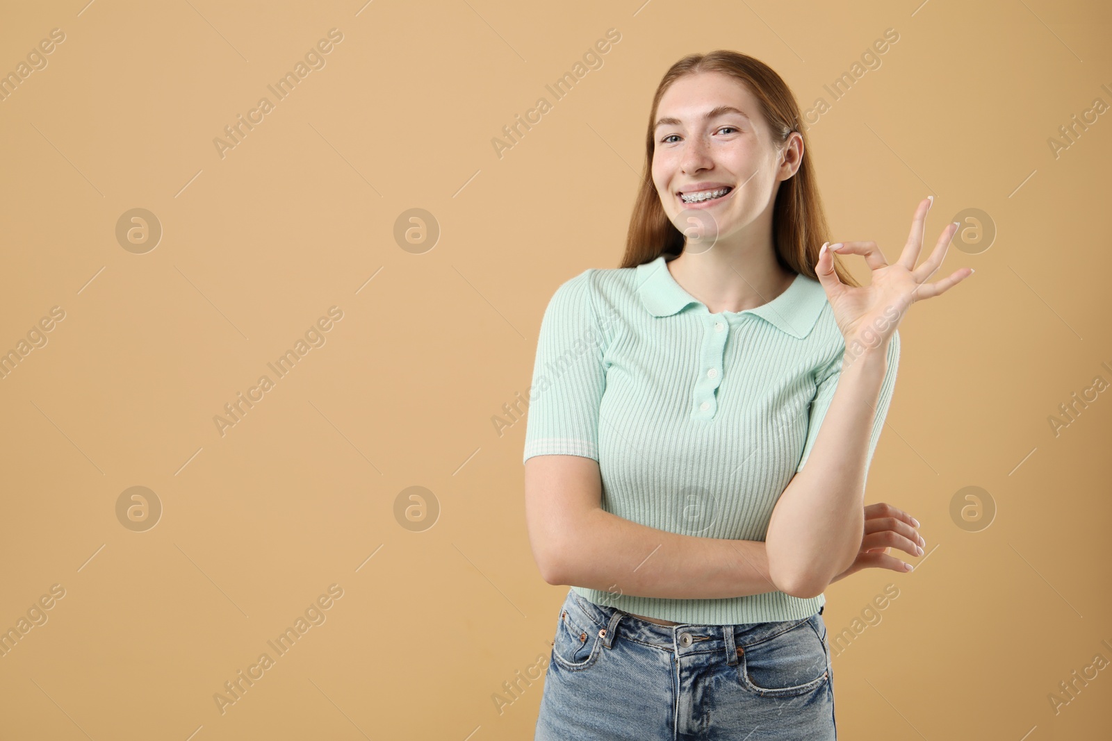 Photo of Smiling girl with braces showing ok gesture on beige background, space for text