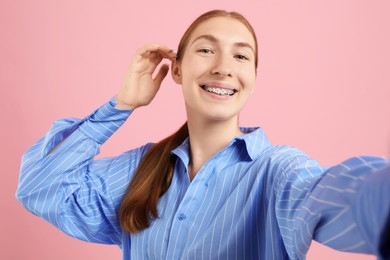 Photo of Smiling girl with braces taking selfie on pink background