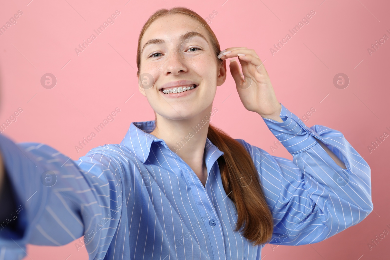 Photo of Smiling girl with braces taking selfie on pink background