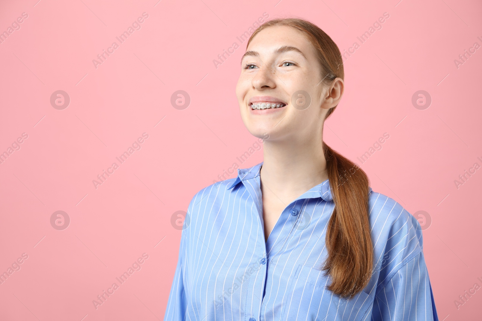 Photo of Smiling girl with braces on pink background, space for text