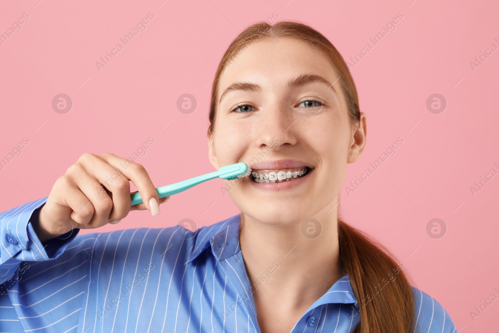 Photo of Girl with braces cleaning teeth on pink background