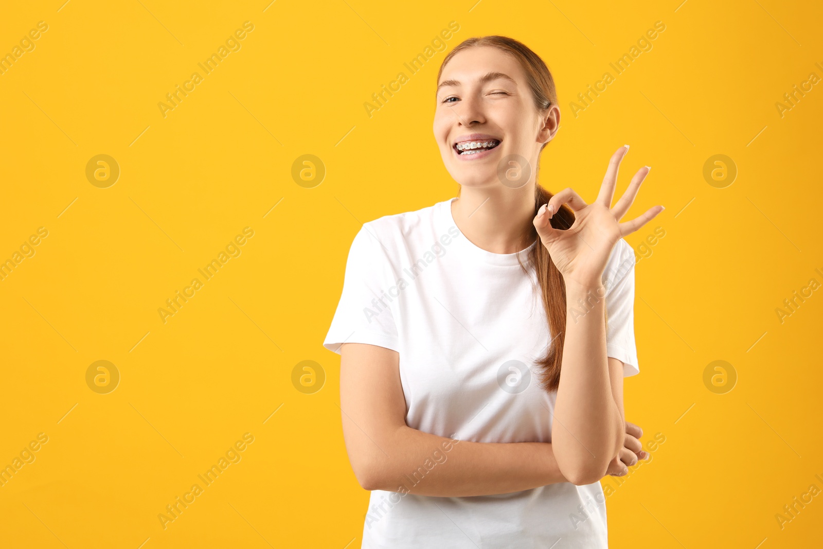 Photo of Smiling girl with braces showing ok gesture on orange background, space for text