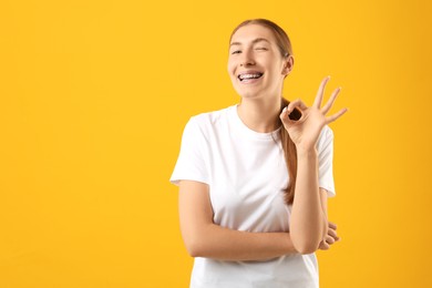 Photo of Smiling girl with braces showing ok gesture on orange background, space for text