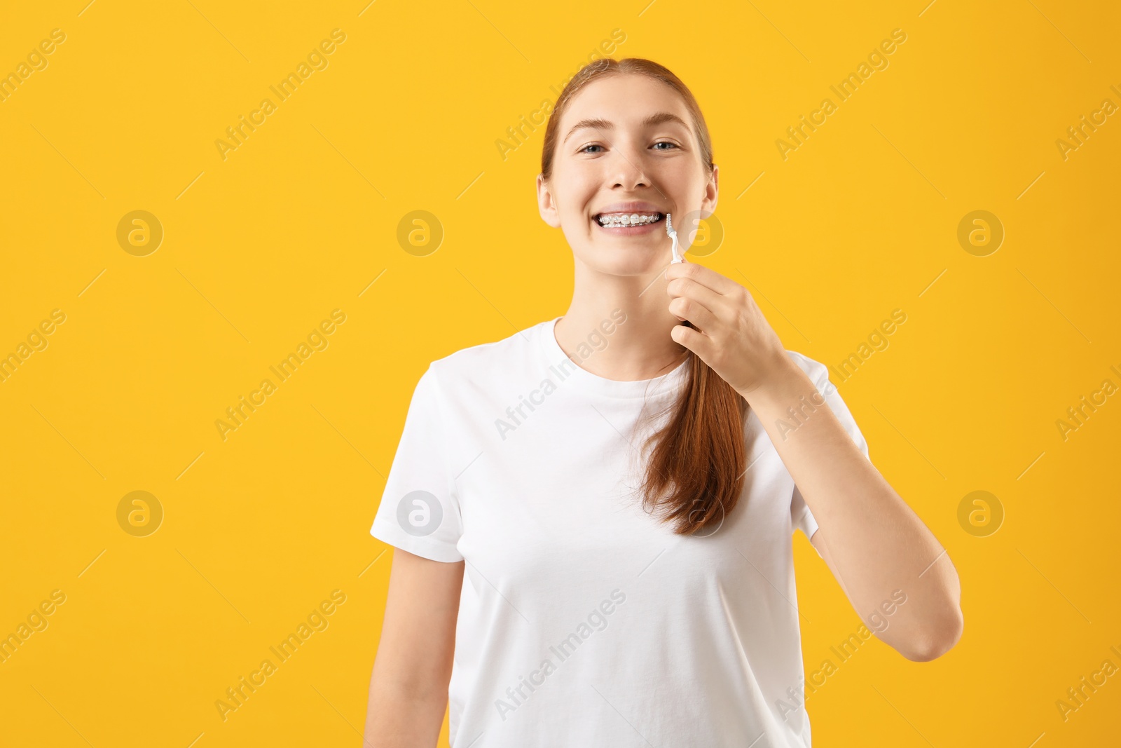 Photo of Girl with braces cleaning teeth with interdental brush on orange background, space for text