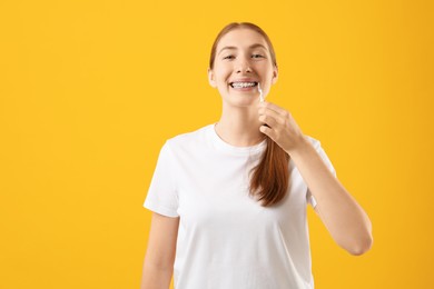 Photo of Girl with braces cleaning teeth with interdental brush on orange background, space for text