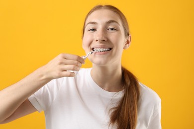 Photo of Girl with braces cleaning teeth with interdental brush on orange background