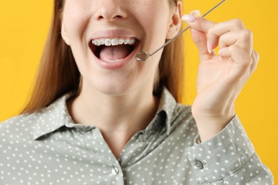 Photo of Girl with braces using dental mirror on orange background, closeup