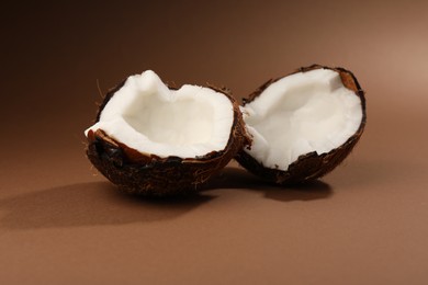 Photo of Halves of cracked coconut on brown background