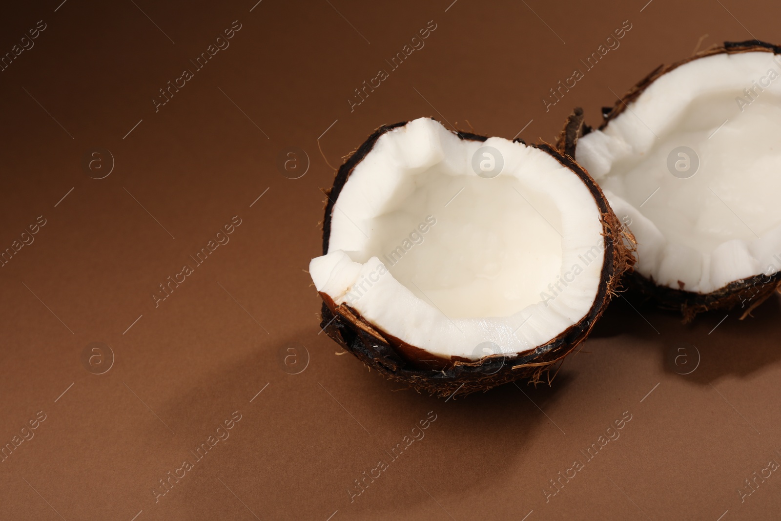 Photo of Halves of cracked coconut on brown background, closeup. Space for text