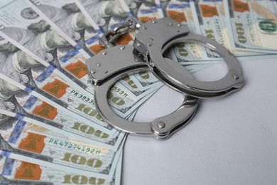 Photo of Corruption concept. Handcuffs and dollar banknotes on grey background, closeup