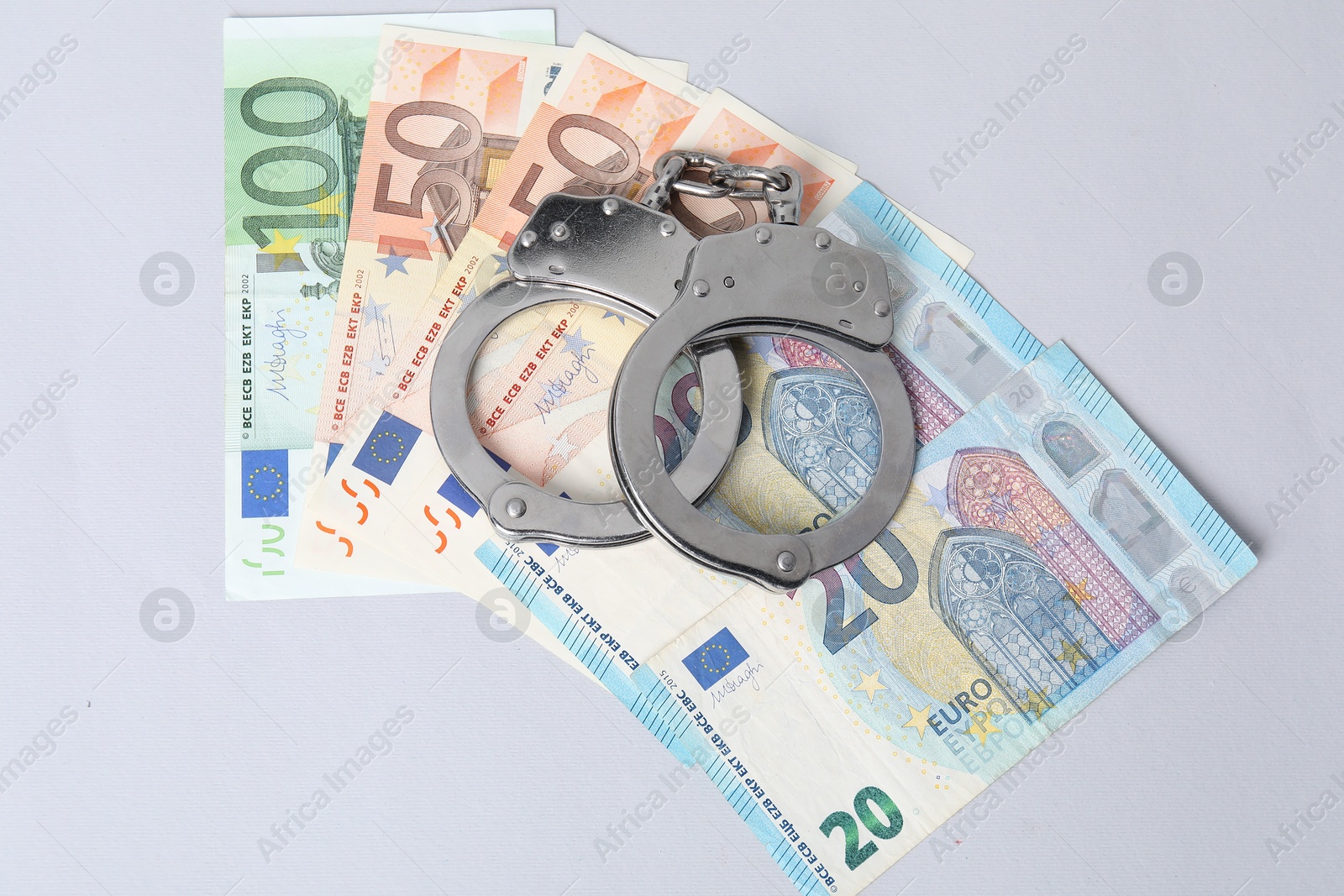 Photo of Corruption concept. Handcuffs and euro banknotes on grey background, top view