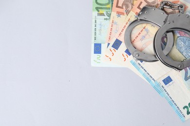 Photo of Corruption concept. Handcuffs and euro banknotes on grey background, top view. Space for text