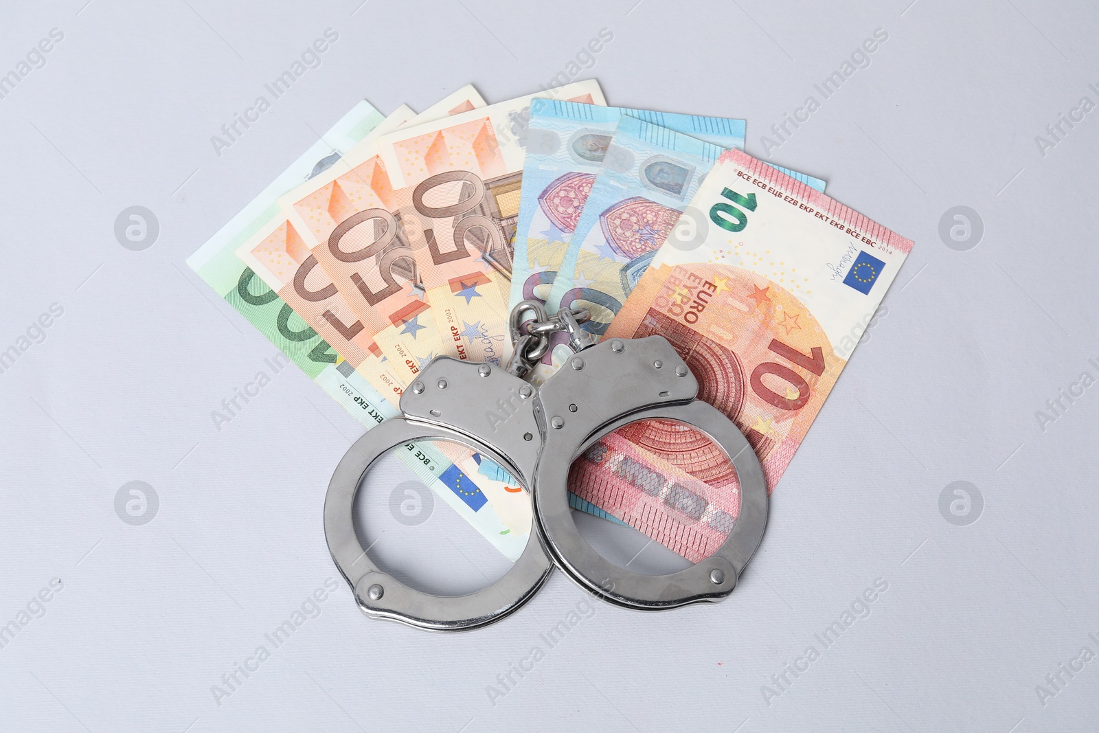 Photo of Corruption concept. Handcuffs and euro banknotes on grey background, top view