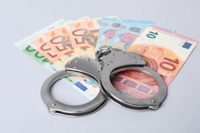 Photo of Corruption concept. Handcuffs and euro banknotes on grey background, closeup