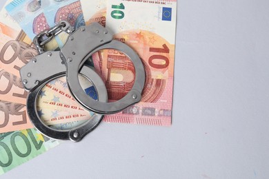 Photo of Corruption concept. Handcuffs and euro banknotes on grey background, top view. Space for text