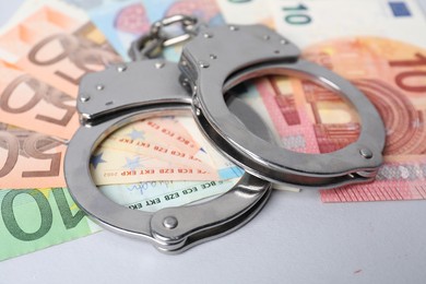 Photo of Corruption concept. Handcuffs and euro banknotes on grey background, closeup