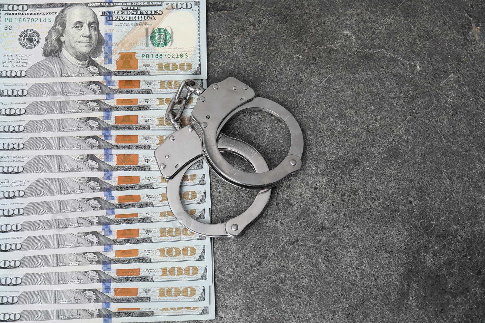 Photo of Corruption concept. Handcuffs and dollar banknotes on grey table, top view. Space for text