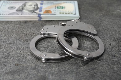 Photo of Corruption concept. Handcuffs and dollar banknotes on grey table, closeup