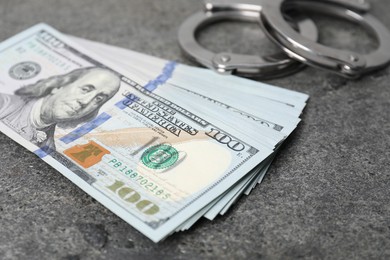 Photo of Corruption concept. Handcuffs and dollar banknotes on grey table, closeup