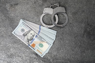 Photo of Corruption concept. Handcuffs and dollar banknotes on grey table, top view