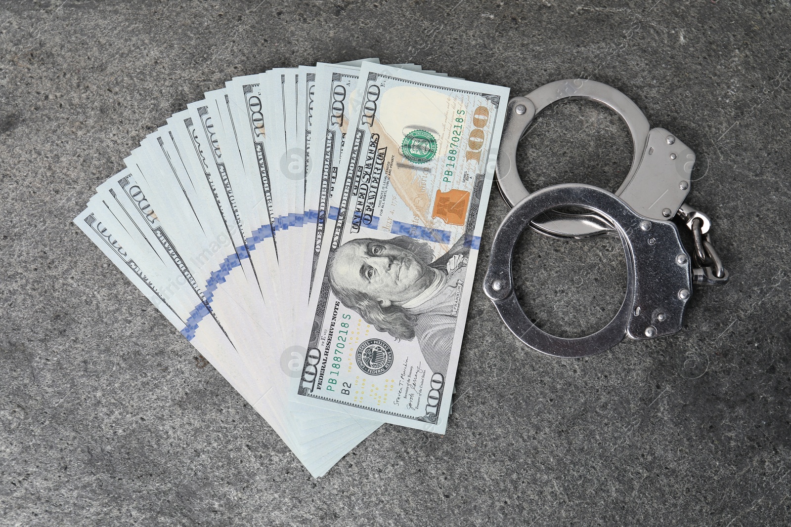 Photo of Corruption concept. Handcuffs and dollar banknotes on grey table, top view