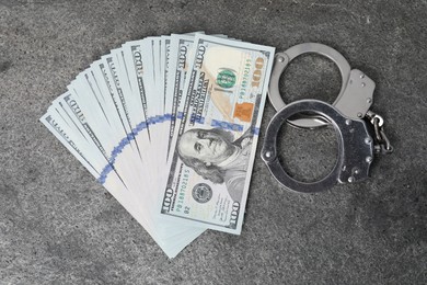 Corruption concept. Handcuffs and dollar banknotes on grey table, top view