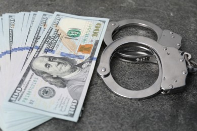 Photo of Corruption concept. Handcuffs and dollar banknotes on grey table, closeup