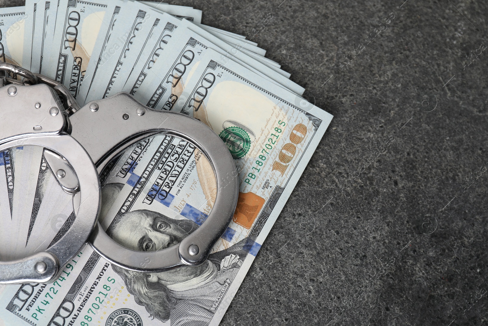 Photo of Corruption concept. Handcuffs and dollar banknotes on grey table, top view. Space for text