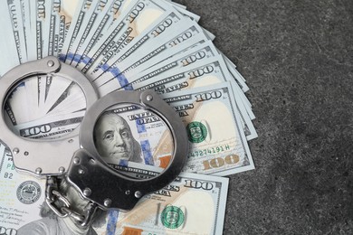 Photo of Corruption concept. Handcuffs and dollar banknotes on grey table, top view