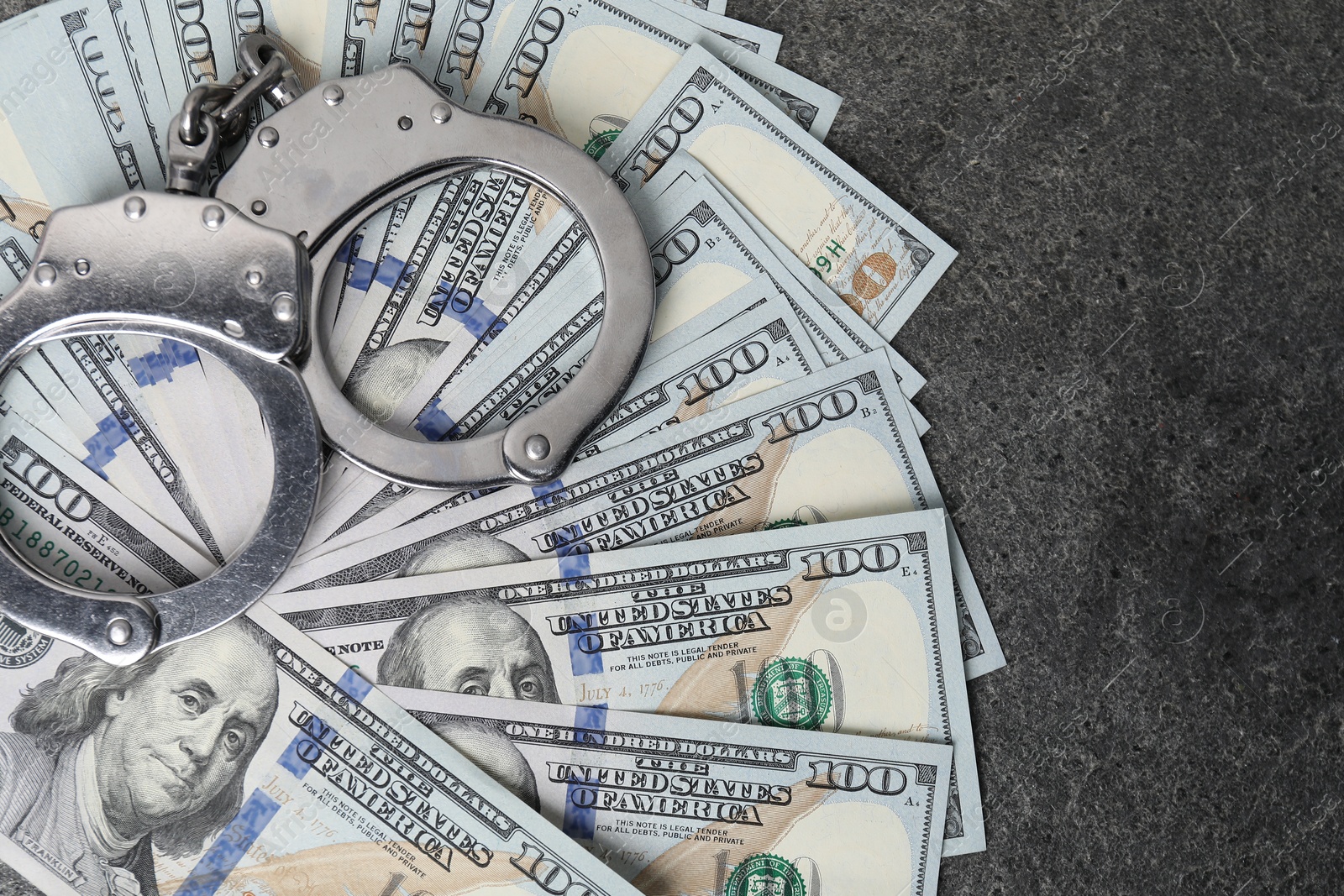 Photo of Corruption concept. Handcuffs and dollar banknotes on grey table, top view