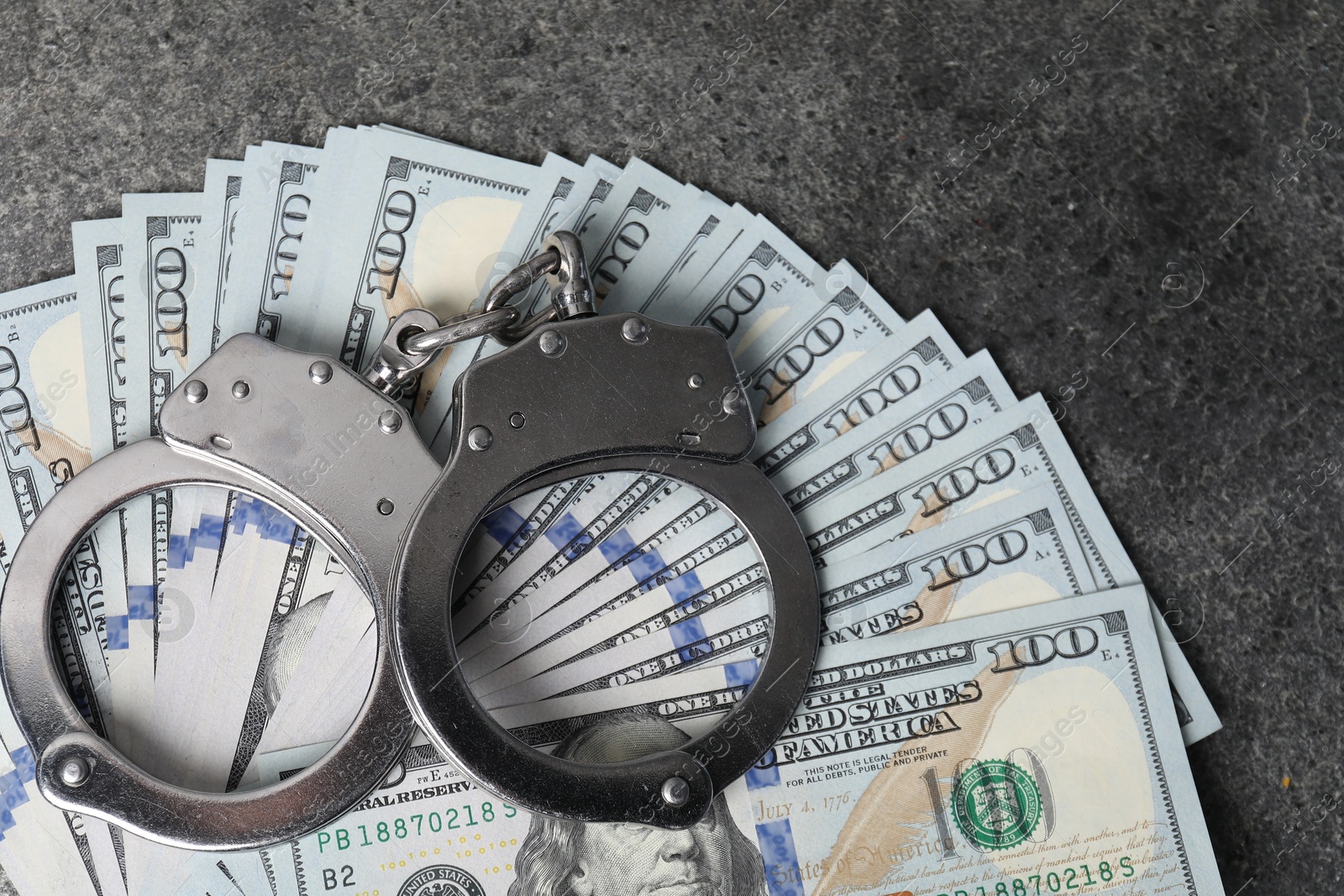 Photo of Corruption concept. Handcuffs and dollar banknotes on grey table, top view