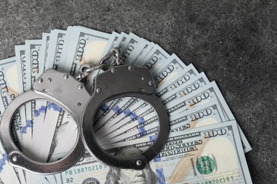 Photo of Corruption concept. Handcuffs and dollar banknotes on grey table, top view