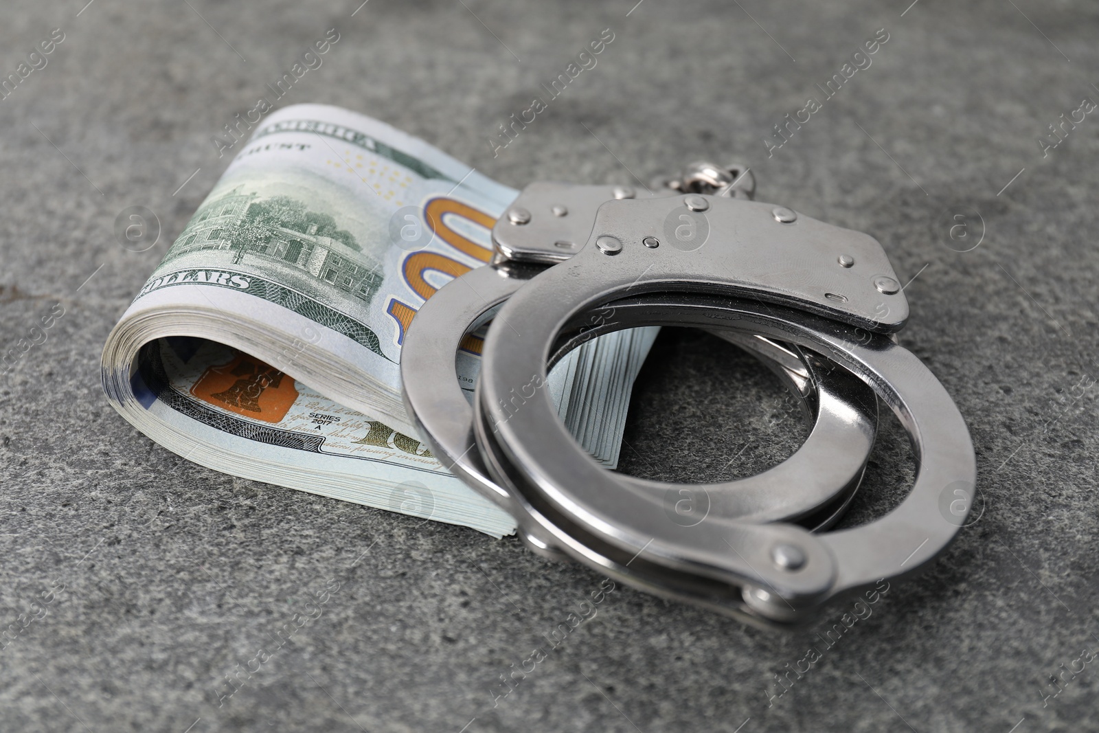 Photo of Corruption concept. Handcuffs and dollar banknotes on grey table, closeup