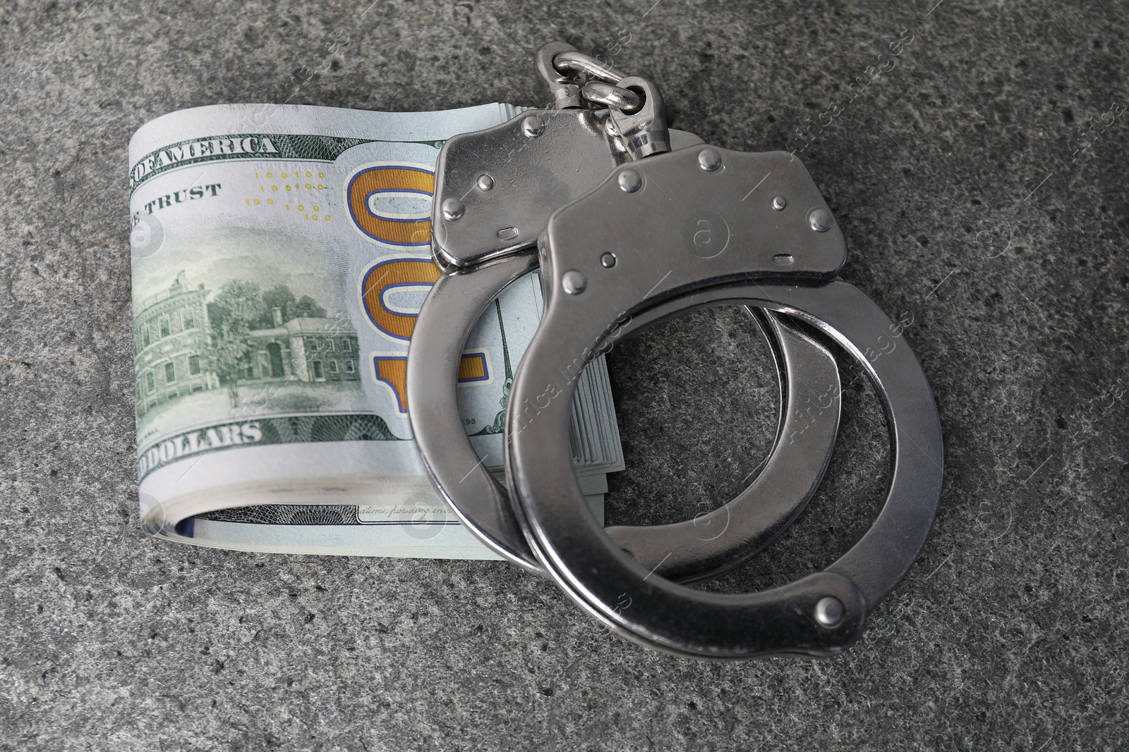 Photo of Corruption concept. Handcuffs and dollar banknotes on grey table, closeup