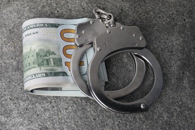 Corruption concept. Handcuffs and dollar banknotes on grey table, closeup