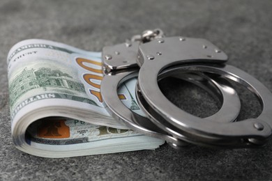 Photo of Corruption concept. Handcuffs and dollar banknotes on grey table, closeup