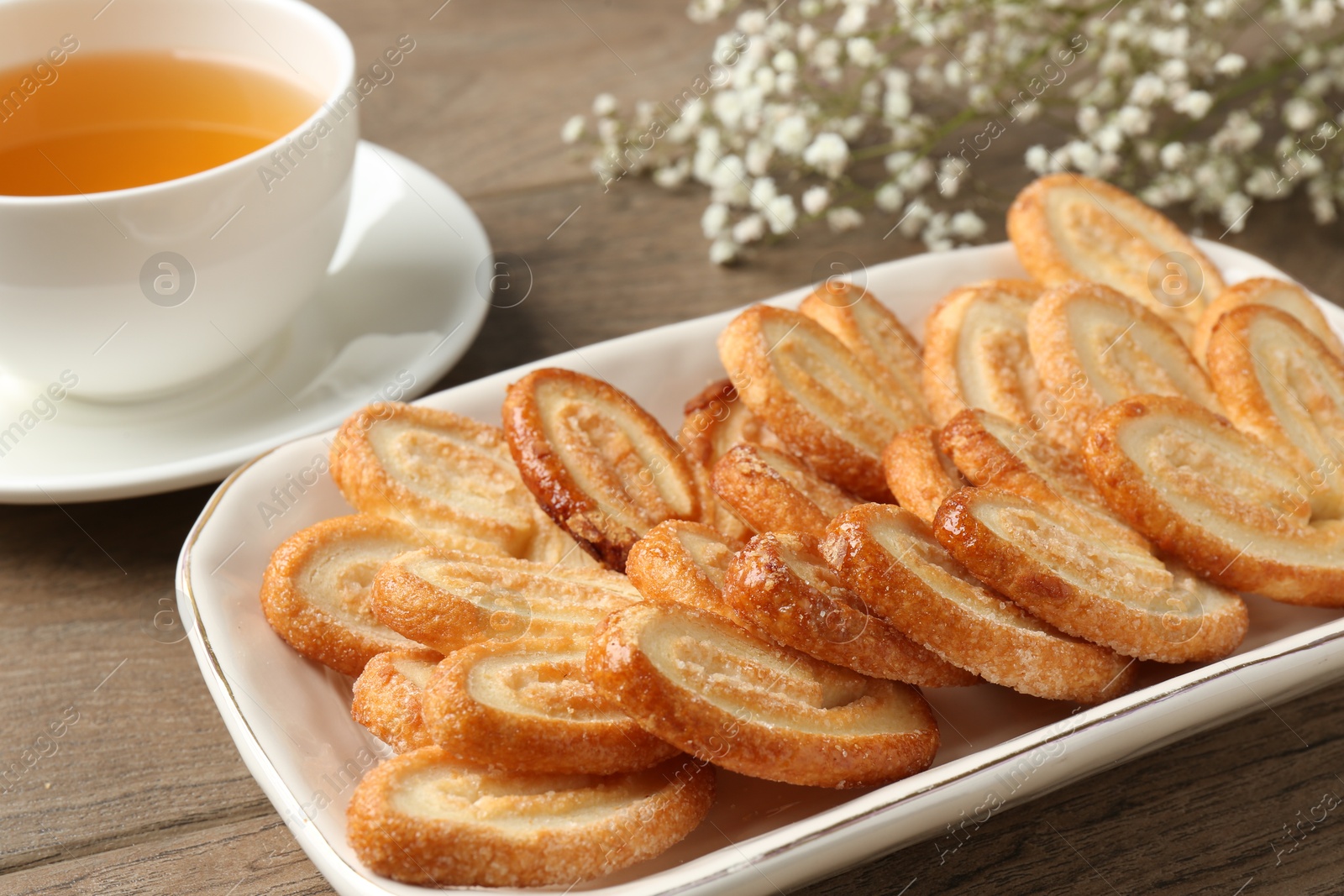 Photo of Tasty french palmier cookies, tea and gypsophila flowers on wooden table, closeup