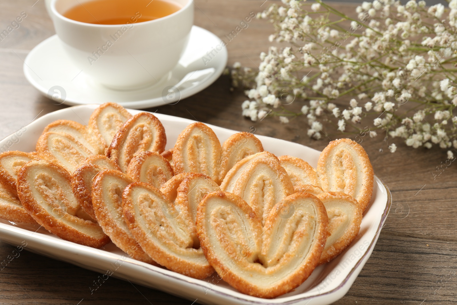 Photo of Tasty french palmier cookies, tea and gypsophila flowers on wooden table, closeup