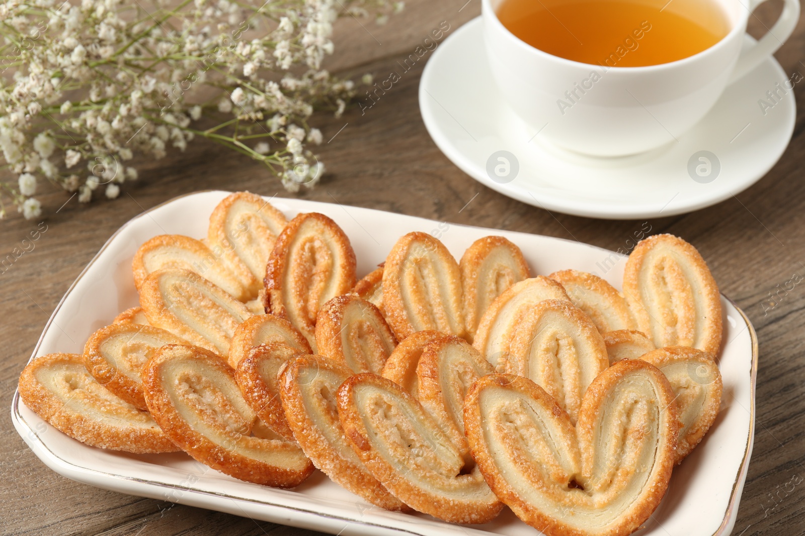 Photo of Tasty french palmier cookies, tea and gypsophila flowers on wooden table, closeup