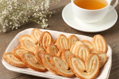 Photo of Tasty french palmier cookies, tea and gypsophila flowers on wooden table, closeup